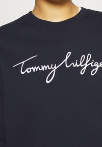 Marineblauwe sweatshirt met een ronde hals en een wit geborduurd "Tommy Hilfiger" logo op de borst. Zacht, gestructureerd materiaal.
