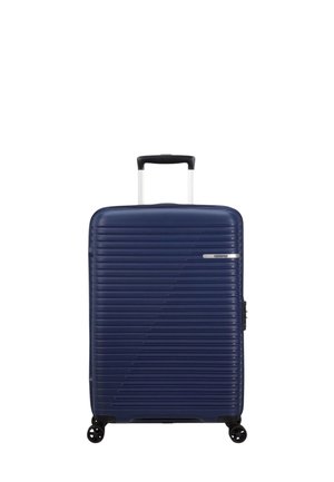 Valigia rigida navy con texture a righe orizzontali, ruote nere e manico estraibile. Presenta una chiusura laterale e un branding minimale.
