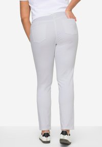 Pantalons gris ajustés avec une texture lisse, poches arrière et une taille standard. Associés à des sneakers blancs et noirs.