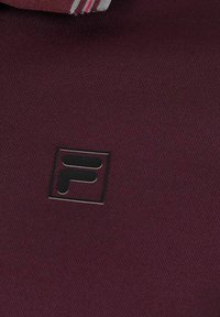 Bordeaux textiel met een zwart, vierkant logo met een prominente letter "F." Zachte textuur, geen zichtbare patronen of extra details.