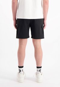 Zwarte cargoshorts met twee zijzakken, rechte snit en lichtgewicht stof. G gedragen met witte sneakers en gestreepte sokken.