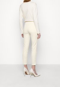 Crème-kleurige slim-fit broek met twee achterzakken, gecombineerd met een lichtgestreepte trui en nude hoge hakken.