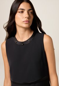 Schwarzes ärmelloses Kleid aus glattem Stoff, mit einem runden Ausschnitt mit schwarzen Perlenakzenten und einem dezenten Taillenband.
