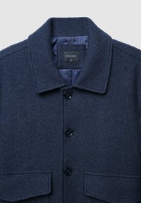Cappotto di lana blu navy con colletto, quattro bottoni neri e due tasche frontali. Presenta un tessuto testurizzato e una fodera interna liscia.