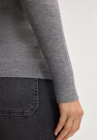 Manica di maglione grigia a coste con orlo semplice, abbinata a jeans grigi scuri con un design della tasca posteriore e dettagli di cucitura sottili.