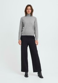 Grauer Rollkragenpullover kombiniert mit lockeren schwarzen Hosen. Das Outfit zeichnet sich durch ein strukturiertes Strickdesign und schwarze Stiefel in Knöchelhöhe aus.