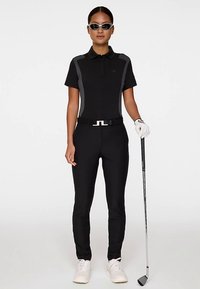 Czarna koszulka polo do golfa z szarymi akcentami, zestawiona z czarnymi spodniami. Dodatki to biały pasek, białe buty, okulary przeciwsłoneczne i kij do golfa.