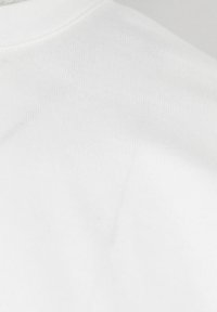 Tessuto di cotone bianco con una consistenza liscia, scollatura rotonda e sottili rigature lungo il colletto e la cucitura della spalla.