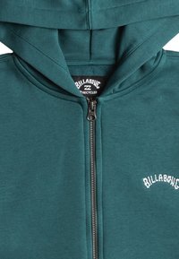 Felpa con zip di colore teal realizzata in materiale riciclato. Presenta un cappuccio con cordino e un logo ricamato bianco sul petto. Texture liscia.