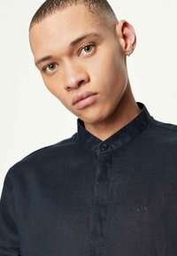 Camicia button-up blu scuro con colletto alla cinese, tessuto testurizzato e dettaglio del logo discreto sul petto. Finitura liscia.