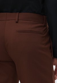 Ruske muške hlače krojene po meri s glatkom teksturom, sa detaljem zadnjeg džepa. Struk je ravan, a tkanina izgleda lagano.