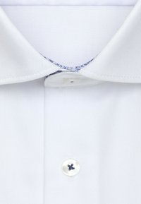 Chemise à col blanc avec une finition texturée, présentant un col intérieur accentué de bleu et une patte de boutonnage simple avec un bouton blanc.