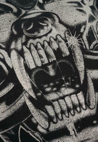 Čierna textília s grafickým dizajnom lebky s viditeľnými zubami, škrabancami a výrazným čierno-bielym kontrastom. Povrch vyzerá drsne.