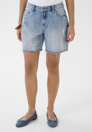 Shorts en denim bleu clair avec ourlets effilochés et patchs déchirés, portés avec des ballerines bleues.