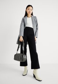 Blazer cinza, blusa branca, calças pretas de cintura alta, botas de tornozelo em marfim e uma bolsa de mão cinza escuro com alça de ombro. Texturas suaves.