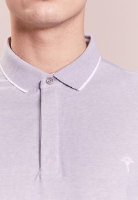 Hellblaues Polohemd mit strukturiertem Kragen und einer Knopfleiste, mit einem kleinen weißen Logo auf der linken Brust.