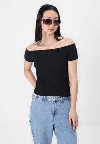 Fekete off-the-shoulder pamut póló, világoskék magas derekú farmernadrággal párosítva. A modellen sötét, oversized napszemüveg van.