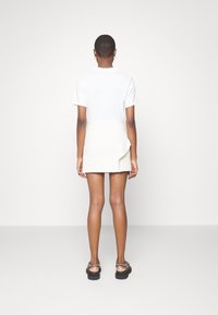 T-shirt bianco a maniche corte abbinato a una mini gonna beige chiaro con design asimmetrico e tessuto leggermente testurizzato. Sandali neri con piattaforma.