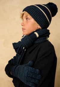 Marineblå strikket hue med pom-pom, matchende tørklæde med striber, og teksturerede handsker, alle i koordinerede mørkeblå nuancer.