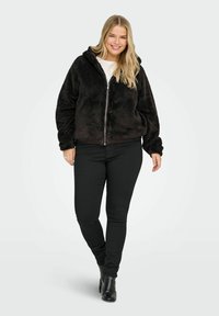 Must musta zip-up kapuutsiga, pehme ja must, seljas valge t-särk ning koos mustade kitsaste pükstega ja plätudega.