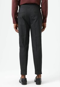 Grijze op maat gemaakte broek met een gladde stoffen textuur, voorzien van achterzakken en opgerolde zomen, gecombineerd met zwarte schoenen.