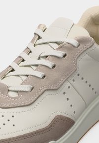 Λευκό δερμάτινο αθλητικό παπούτσι με μπεζ σουέντ στρώσεις, λευκά κορδόνια και διάτρητες λεπτομέρειες στο πλάι για αερισμό και στυλ.