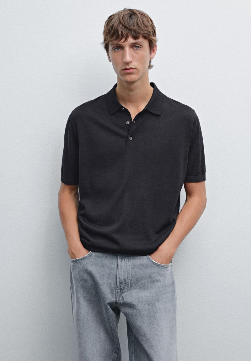 Černé krátké polo tričko s klasickým límcem, s hladkou texturou a zapínáním na tři knoflíky, kombinované se světlými šedými džíny.