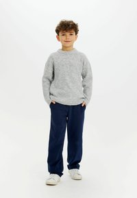 Maglione grigio chiaro a maglia con collo rotondo, abbinato a pantaloni larghi di un blu navy scuro. Modello con sneakers bianche. Outfit semplice e casual.