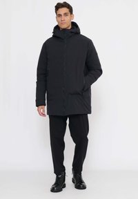 Schwarze isolierte Jacke mit Reißverschluss und Kapuze, kombiniert mit locker sitzender schwarzer Hose und schwarzen Schnürstiefeln. Einfaches, funktionelles Design.
