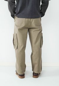 Beige cargobroek met zijzakken, rechte snit en stevige katoenen stof. Heeft een relaxte pasvorm en zichtbare achterzakken.