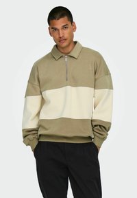Olive green and cream color-blocked pullover sweatshirt with a high collar and quarter zipper; soft, textured fabric with loose sleeves.