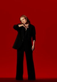 Blazer negro de corte ajustado y pantalones de pierna ancha sobre un fondo rojo. La tela parece suave, con hardware mínimo y líneas limpias.