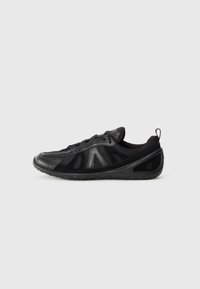 Sneaker nera caratterizzata da una combinazione di pannelli lisci e testurizzati, rete traspirante e suola in gomma flessibile. Il design include dettagli minimi.