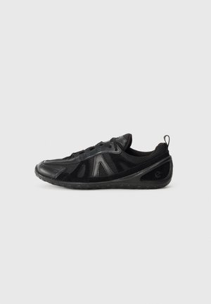 Sneaker nera caratterizzata da una combinazione di pannelli lisci e testurizzati, rete traspirante e suola in gomma flessibile. Il design include dettagli minimi.