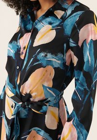 Kukallinen mekko kevyestä kankaasta, jossa on mustan, sinisen, vaaleanpunaisen ja keltaisen värin sekoitusta, sidottava vyö ja napit.