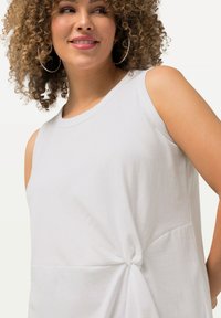 Witte mouwloze top van zachte stof, met een geknoopte detail aan de zijkant en een relaxte silhouet. Gladde textuur en geen patronen.