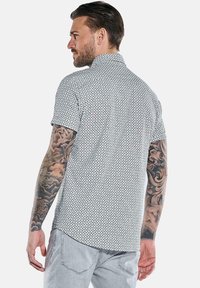 Kurzärmliges Hemd mit Knopfverschluss in einem schwarz-weißen geometrischen Muster, ausgestattet mit einem Kragen und einer lockeren Passform.