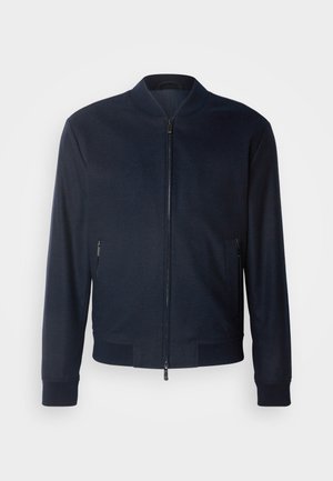 Jūras flotes bumbvedēja jaka, ar rāvējslēdzēju priekšā, ribota apkakle un aproces, sānu kabatas, gluda auduma tekstūra, minimālisma stils, nav redzamu rakstu vai akcentu.