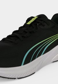 Μαύρο παπούτσι για τρέξιμο Puma με πράσινες και μπλε ρίγες, μαύρα κορδόνια και λευκή σόλα, που δείχνει μπροστινές και πλευρικές λεπτομέρειες.