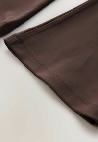 Nahaufnahme von braunen Stoff-Leggings, die eine glatte Textur und doppelt genähte Säume entlang des Saums auf einer hellen Oberfläche zeigen.