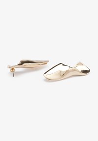 Orecchini a forma di scarpa in tono dorato con superficie lucida e chiusura a perno. Design curvo con finitura liscia e linee eleganti.