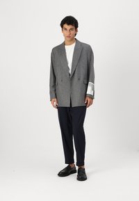 Blazer dublu din tartan gri cu rever ascuțit, purtat cu un tricou alb și pantaloni bleumarin, asortat cu pantofi negri.