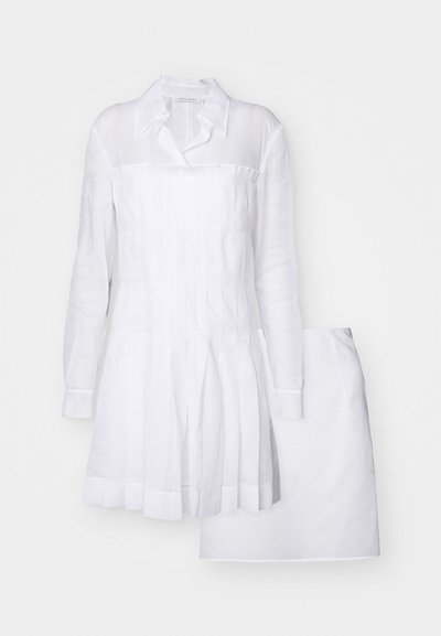 Abito bianco in lino con maniche lunghe, colletto a bottoni e design plissettato. La gonna è a linea A e il tessuto appare leggero e testurizzato.