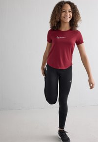 Red athletic t-shirt with logo, paired with black leggings featuring Nike swoosh. Smooth fabric, fitted style, and relaxed silhouette in motion.