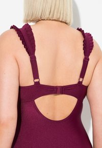 Maillot de bain une pièce bourgogne avec des bretelles à volants, un dos ouvert, des attaches réglables et une texture lisse et brillante.