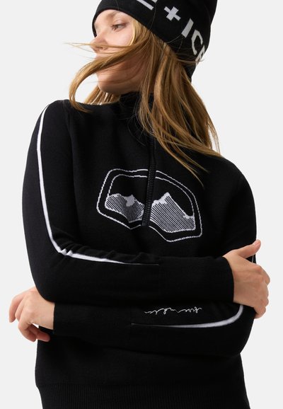 Fekete kötött pulóver magas nyakkal, hegy motívummal és fehér csíkos díszítéssel a karokon. Puha tapintású és testhez simuló kialakítású.