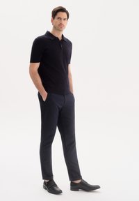 Granatowa koszulka polo z krótkim rękawem, zestawiona z ciemnymi spodniami i czarnymi skórzanymi butami. Posiada klasyczny kołnierzyk oraz dopasowany krój.