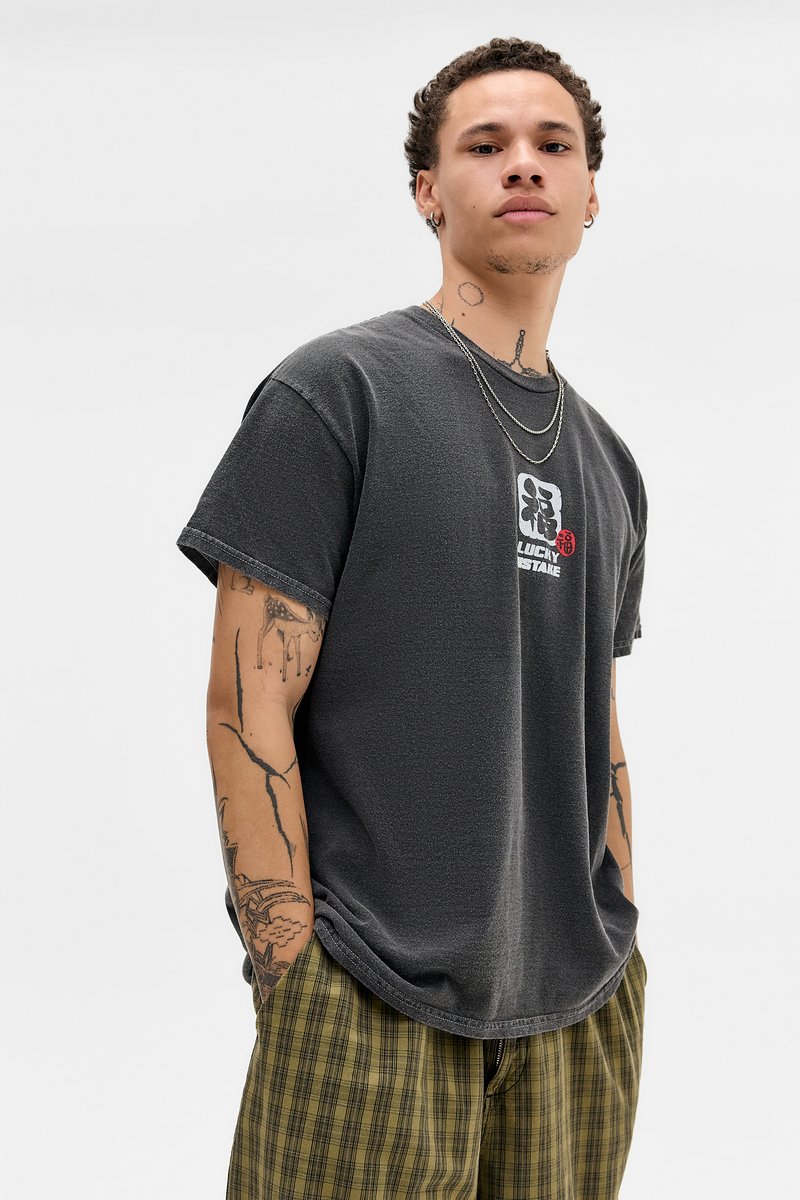 Szürke, nagyméretű póló texturált felülettel és grafikával az elején. Kockás, laza szabású zöld nadrággal párosítva.