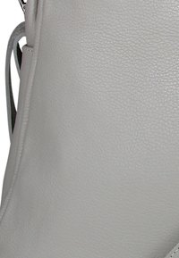 Grijze leren tas met een gestructureerd oppervlak, met een gladde vorm en zichtbare stiksels. Beschikt over een zwarte riem aan één kant.