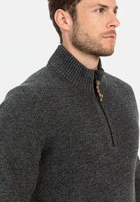 Dunkelgrauer Pullover mit hochgestelltem Rippkragen und Viertelreißverschluss, ausgestattet mit einem strukturierten Strickmuster und einem subtilen gelben Akzent am Reißverschluss.